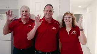 Three people in red polo shirts waving at the camera in a bright hallway.