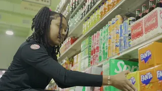 Young person with braided hair reaching for Fanta bottles on a supermarket shelf, selecting a drink.