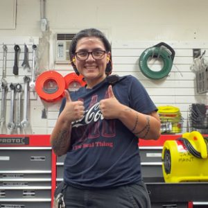 Person in a workshop giving two thumbs up, with tools on a pegboard and a red tool chest visible in the background.