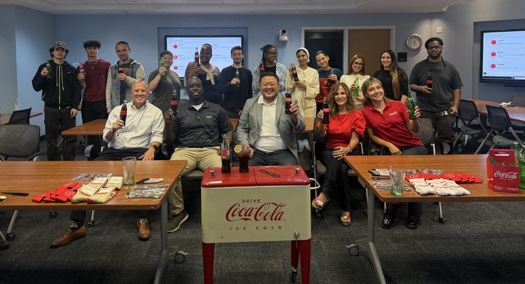 perfect-pour-FIU-4 - Coca-Cola Beverages Florida Group of coworkers in a meeting room smiling and holding Coca-Cola bottles for a company gathering.