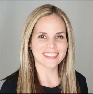 Head-and-shoulders portrait of a smiling woman with long blonde hair, wearing a black top against a neutral background.
