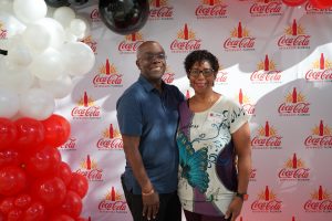 Smiling couple posing in front of a Coca-Cola backdrop with white and red balloon decorations.