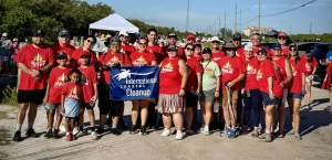 Group of volunteers in red Coca-Cola shirts posing outdoors with an International Coastal Cleanup banner at a sunny event site.